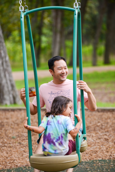 Dad and child swinging together joyfully on a swing set. 